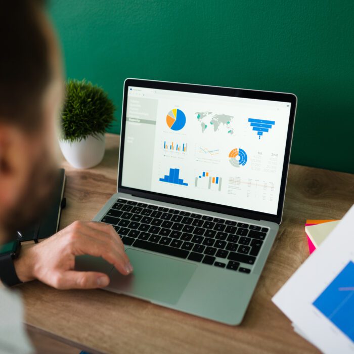 Rear view of a young man working on his laptop and looking at a work report and graphs