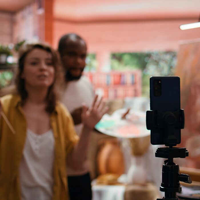 Woman artist hosting online class to present products and technique used on rustic artwork, recording tutorial online. Team of painters doing master class for e learning, art instruction. Camera B.